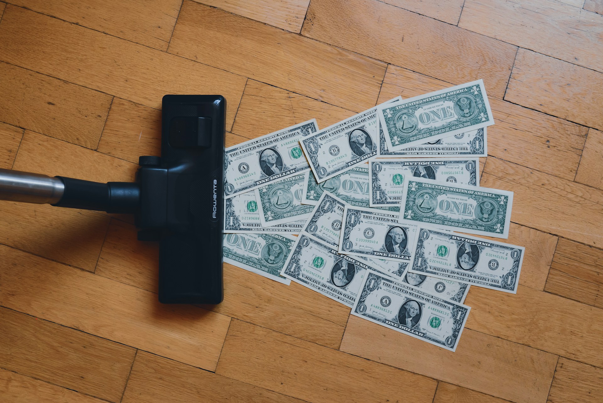 A pile of money on floor being sucked into a vacuum cleanr