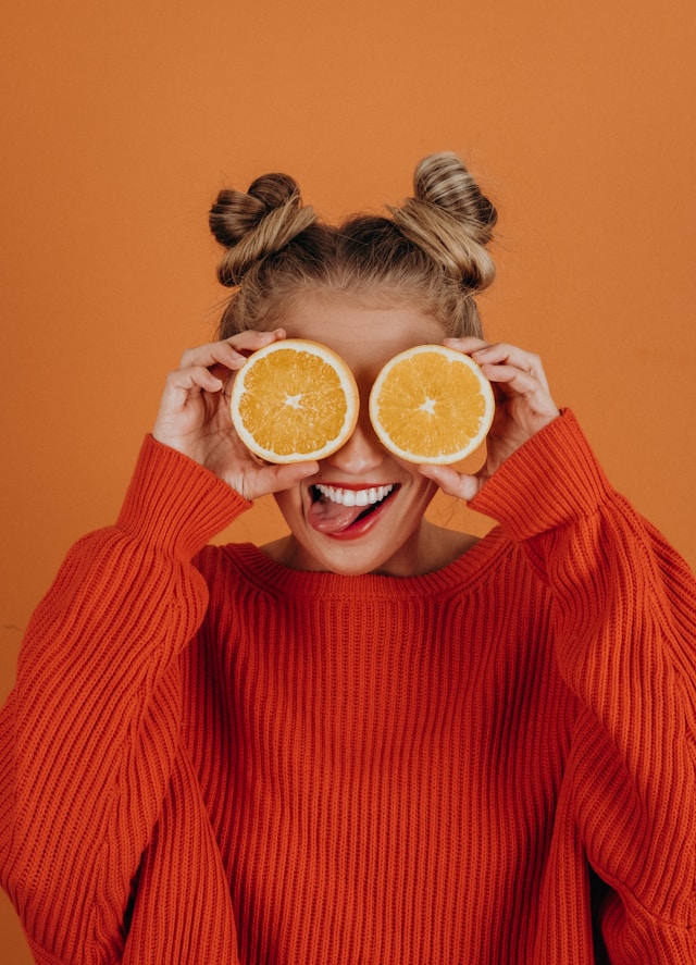 woman holding orange slices to her eyes